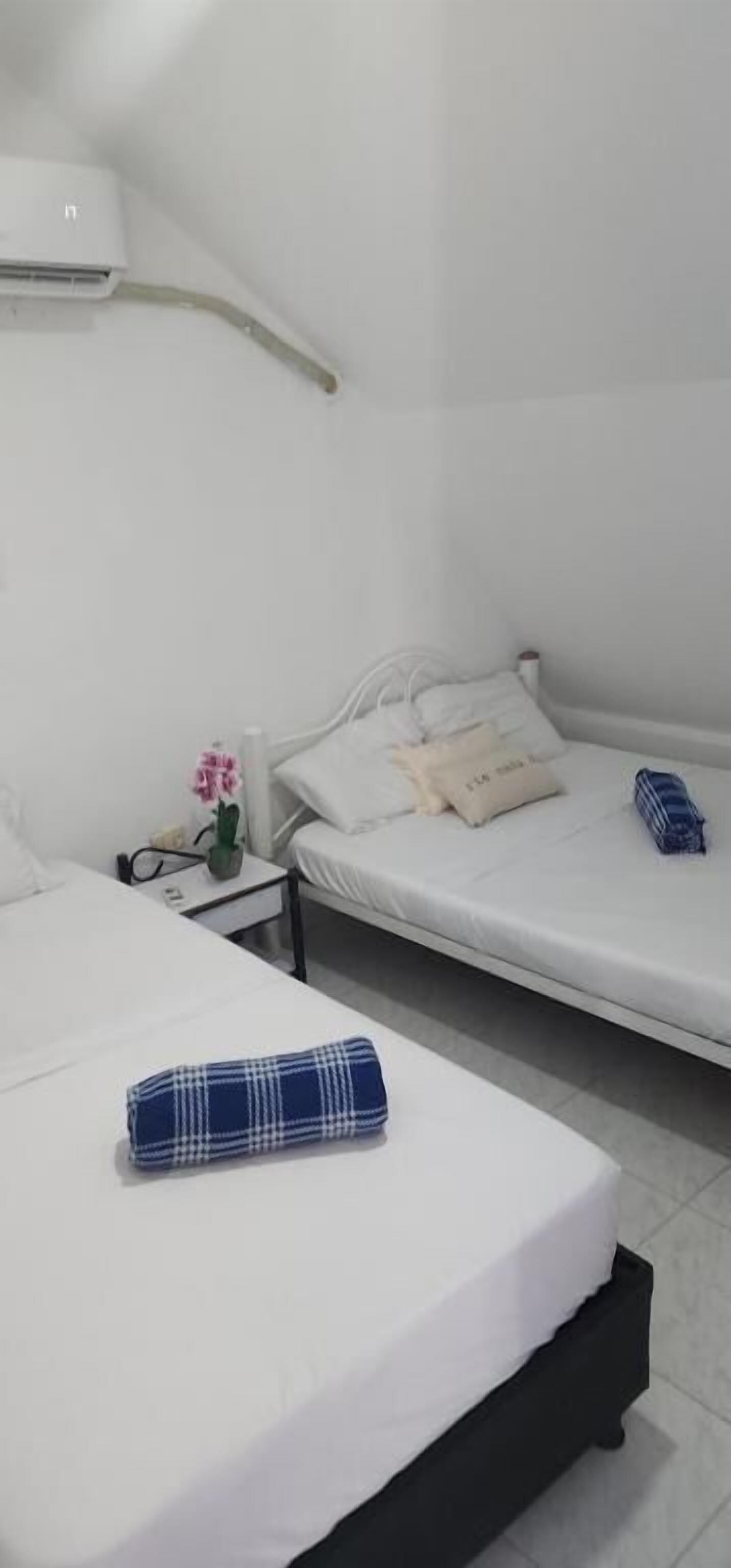 A hotel room with two beds, a bedside table with a lamp, and a wall-mounted air conditioner.
