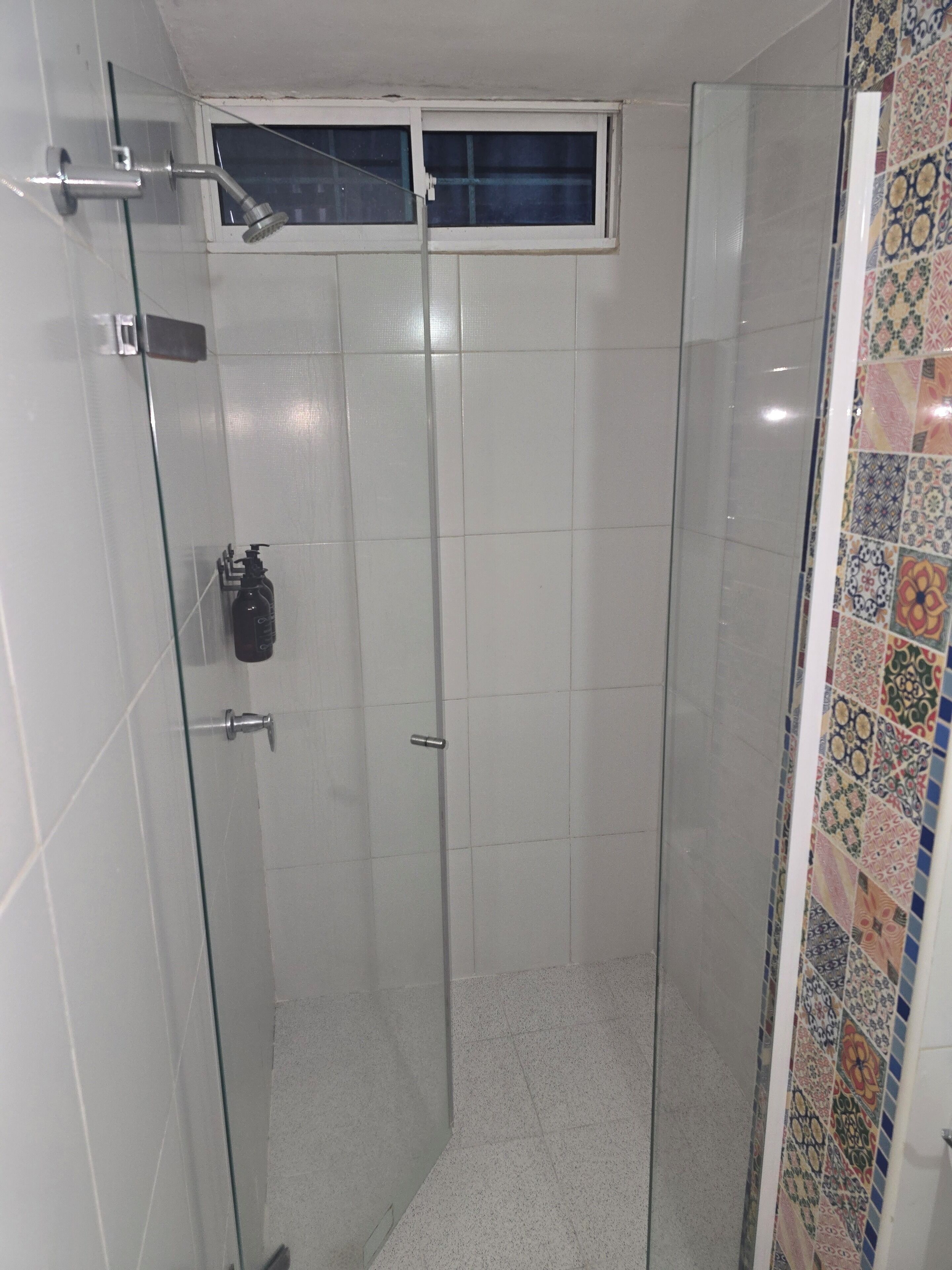 A glass-enclosed shower stall with a window above, tiled walls, and a tiled shower door.