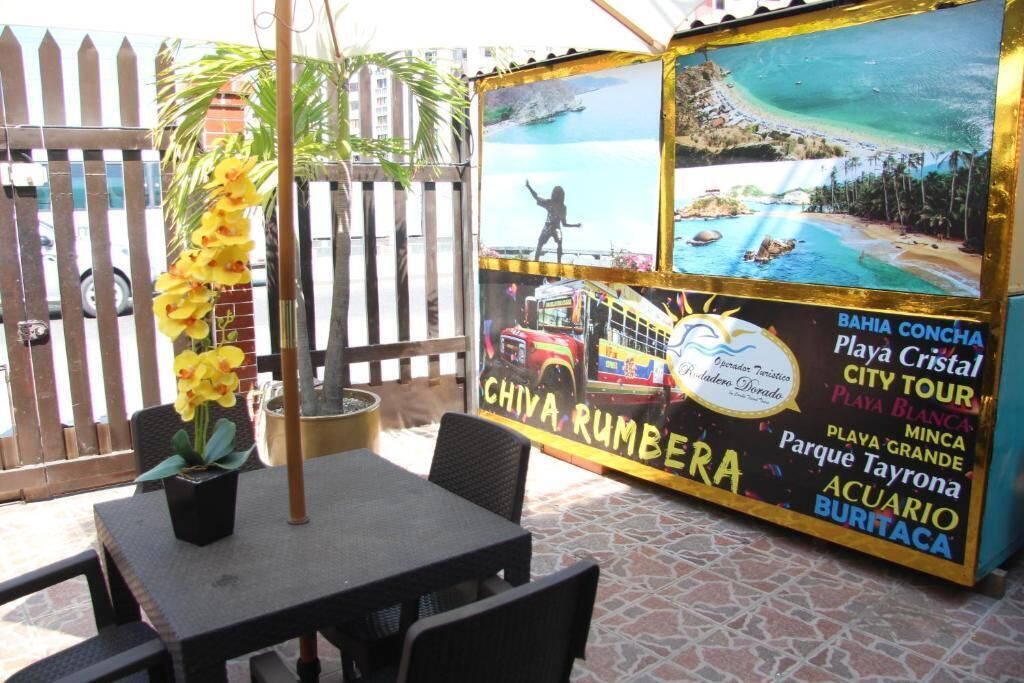 An outdoor seating area with a table and chairs, a potted plant, and a signboard with images of a beach and city tour.
