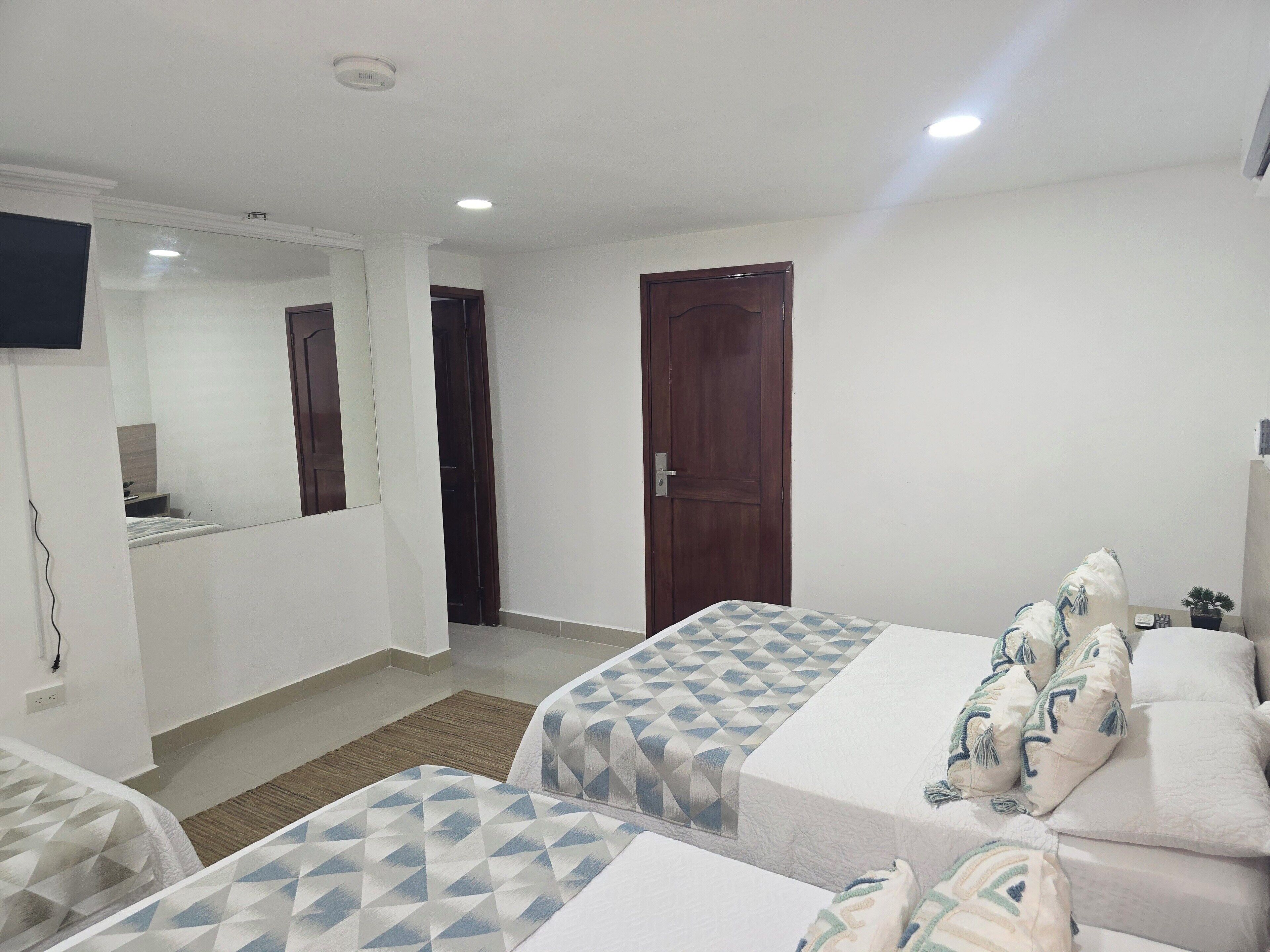 Une chambre d’hôtel avec deux lits, un téléviseur fixé au mur et une porte en bois.