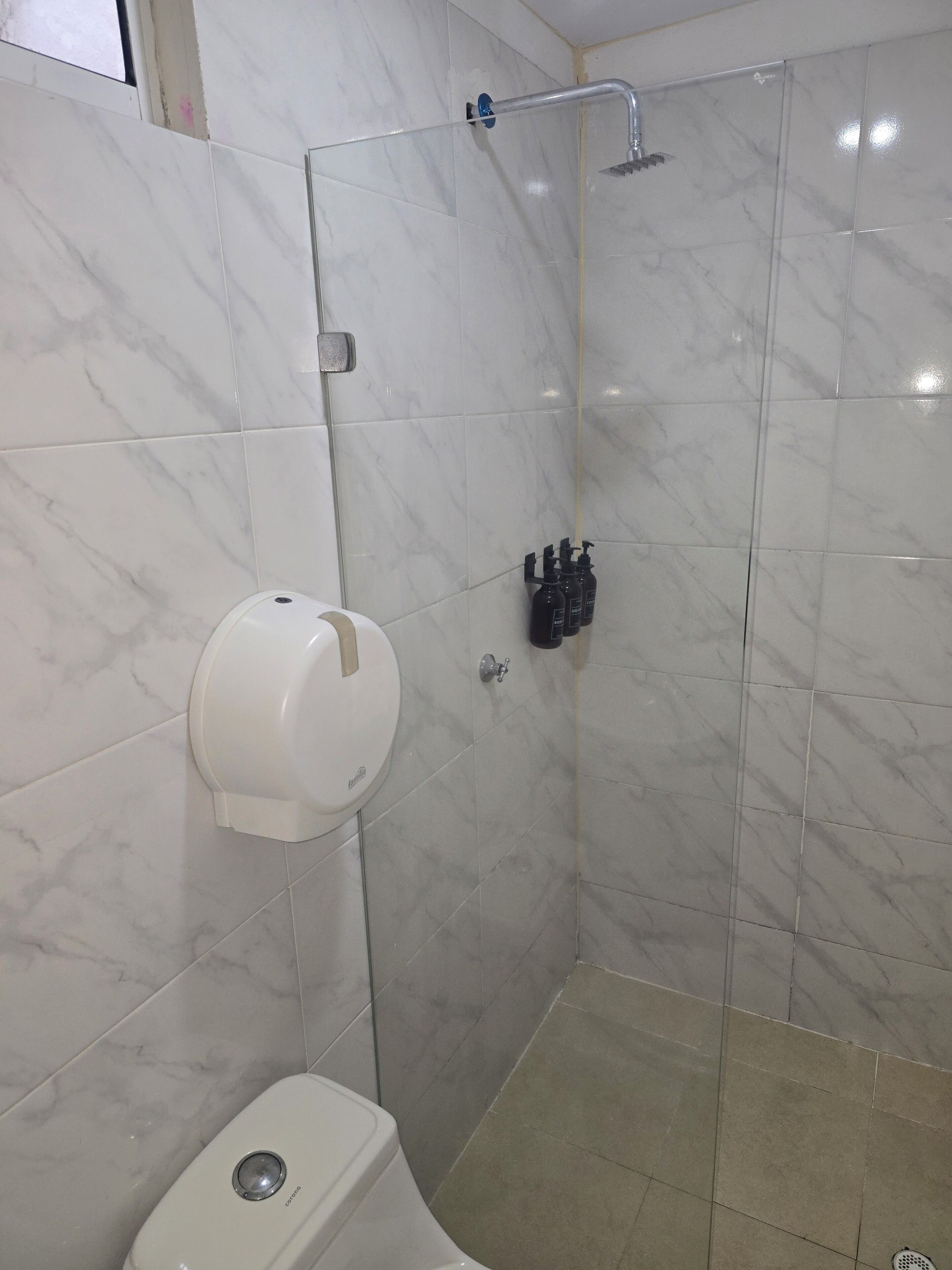 A bathroom with a toilet, a hand dryer, and a shower area with a handheld showerhead.