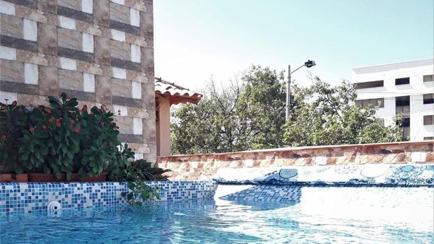 A swimming pool with blue mosaic tiles, surrounded by a stone wall and greenery. - Hotel Rodadero Dorado (Santa Marta)