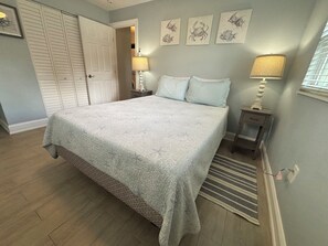 Ein Schlafzimmer mit Bett, Nachttisch, Lampe, Teppich und Bildern an der Wand.