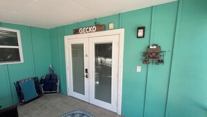 A teal-walled room with a double door labeled "GECKO," a small birdcage, and a patterned rug on the floor.