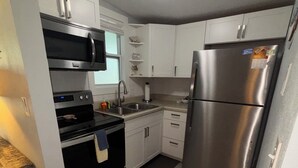 A compact kitchen with white cabinets, a stainless steel refrigerator, a microwave, an oven, and a sink.