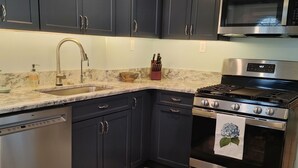 A modern kitchen with dark cabinets, stainless steel appliances, a marble countertop, and patterned rugs. - A Dennis Port gem-just steps to the beach! Totally remodeled top to bottom!    (Dennis)