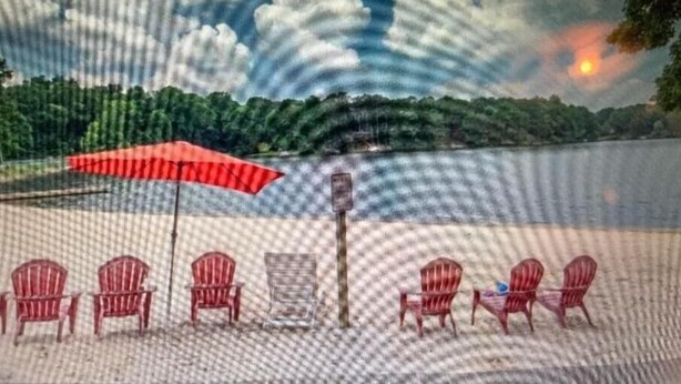Une scène de plage avec une rangée de chaises rouges et un parasol rouge, un poteau en bois, et un coucher de soleil en arrière-plan.