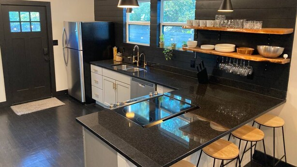 A modern kitchen with a black countertop, stainless steel appliances, and wooden bar stools. - Party walk 3 minute/ Downtown 5 minutes away/ Spring break at Pearl. (San Antonio)