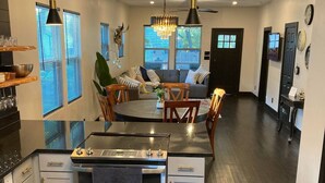 A modern kitchen with a central island, built-in oven, and white cabinetry. There is a dining area with a round table and chairs, and a living room with a sofa and a large window. - Party walk 3 minute/ Downtown 5 minutes away/ Spring break at Pearl. (San Antonio)