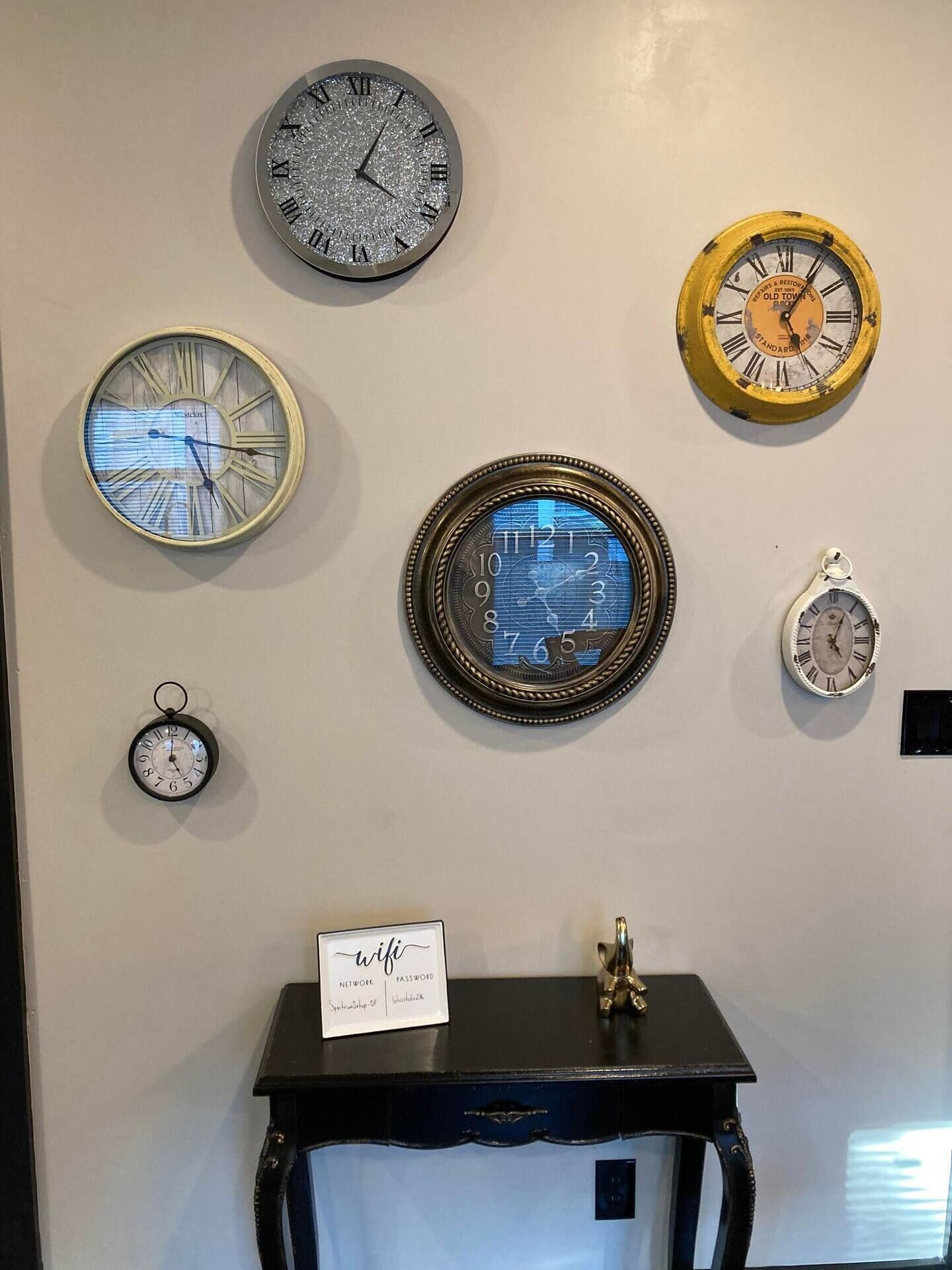 Een muur met verschillende klokken, een kleine tafel met een bordje en een decoratief object.