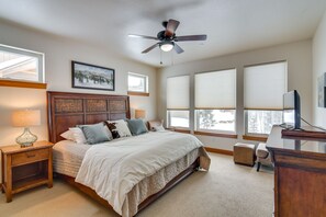 Un dormitorio con cama de madera, ventilador de techo y ventanas grandes con persianas.