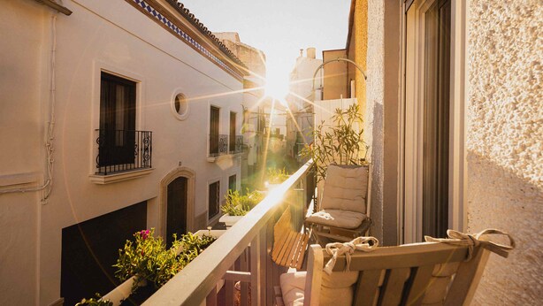 A balcony with a wooden chair and potted plants, overlooking a narrow street with buildings. - Nomadara - Boutique B&B (Coin)