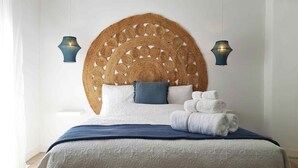A bed with a woven headboard, two wall-mounted lamps, and a stack of towels. - Nomadara - Boutique B&B (Coin)