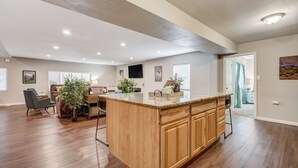 Un vaste espace de vie comprenant un îlot central en bois, un téléviseur à écran plat fixé au mur et un coin repas avec une table et des chaises.