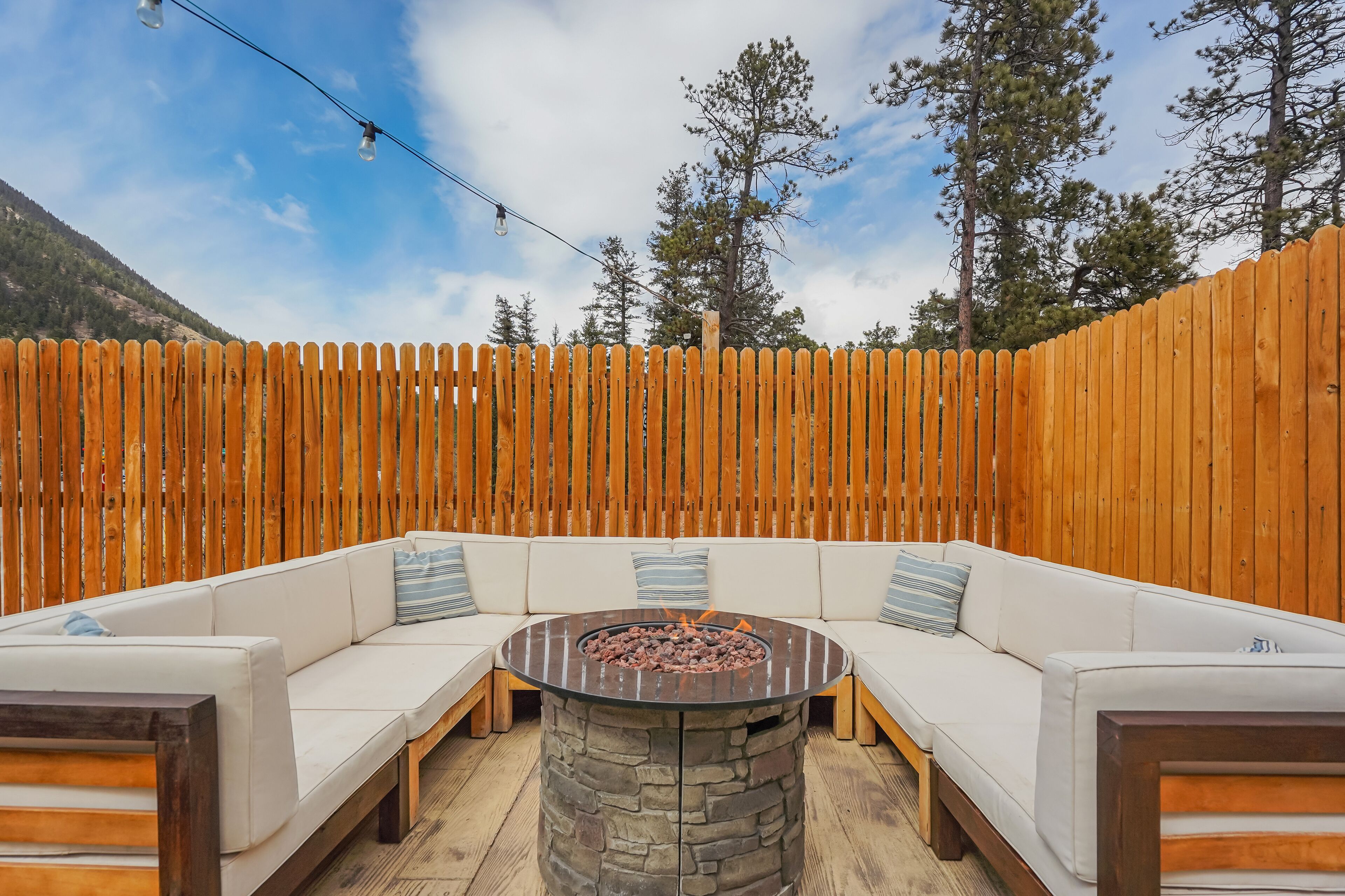 A wooden fence, a stone fire pit, and a white sectional sofa with pillows.