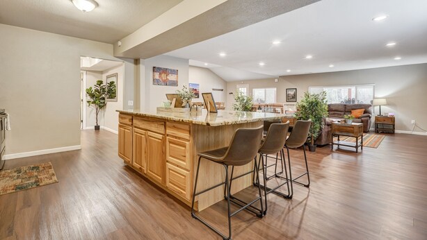 Un vaste espace de vie comprenant un îlot de cuisine, des meubles de rangement en bois et un coin bar avec des tabourets.