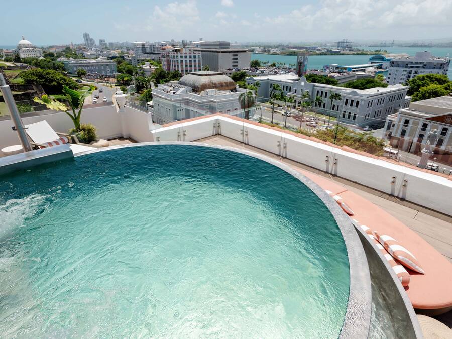 A rooftop pool with a curved edge, surrounded by lounge chairs and a cityscape view.