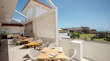Ein Restaurant mit Terrassensitzgelegenheiten, weißen Korbstühlen und Blick auf ein historisches Gebäude.