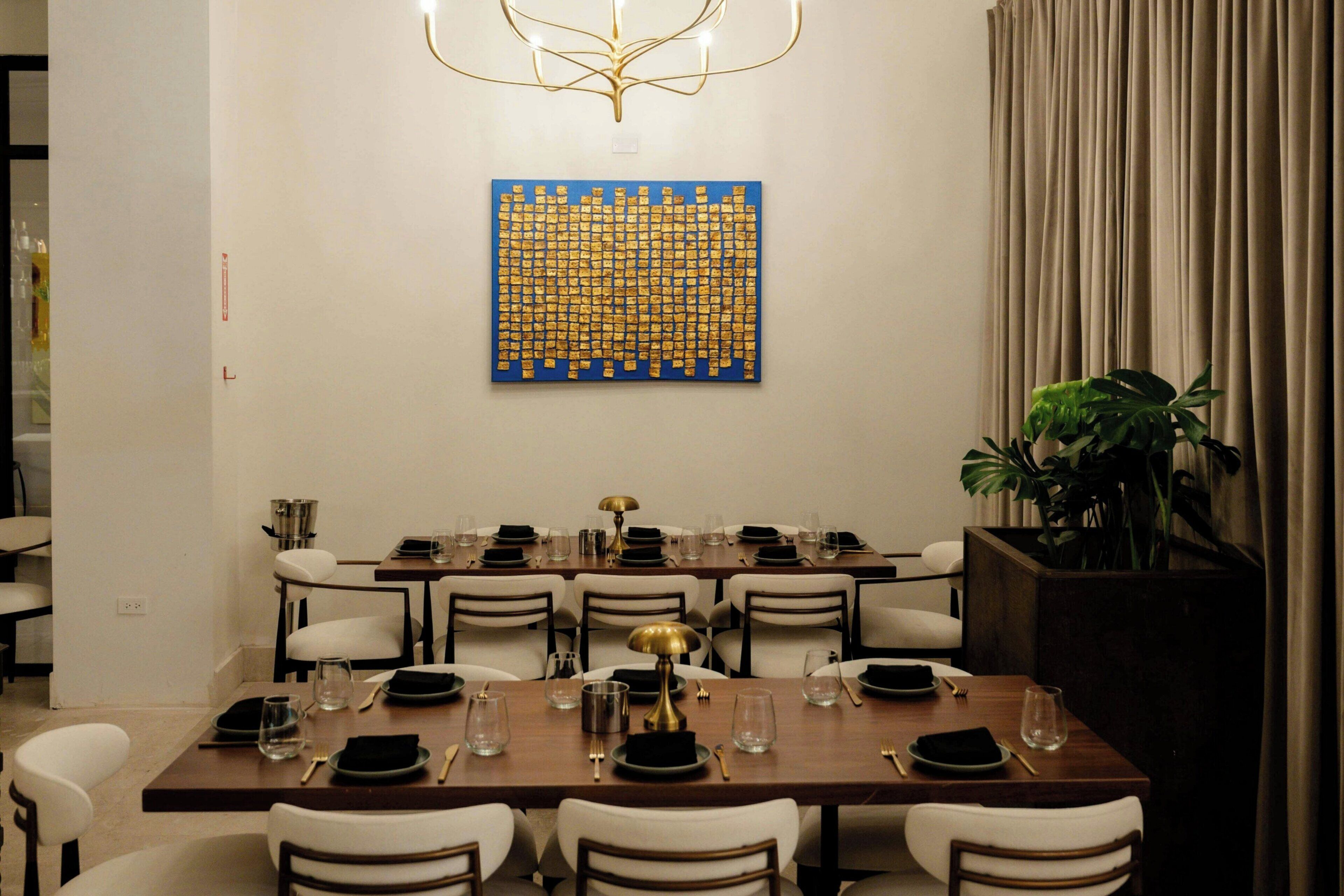 A dining area with a long table set for multiple guests, a decorative wall piece, and a plant.