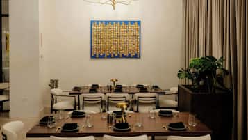 A dining area with a long table set for multiple guests, a decorative wall piece, and a plant.