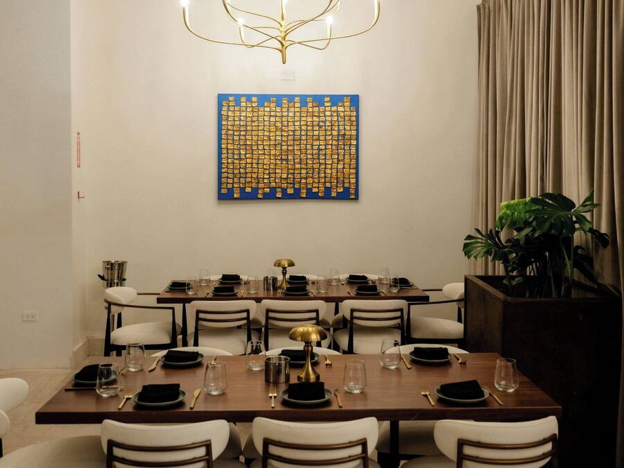 A dining area with a long table set for multiple guests, a decorative wall piece, and a plant.