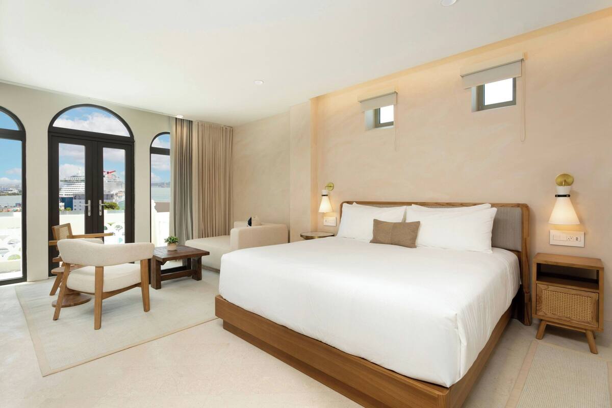 Ein modernes Hotelzimmer mit einem großen Bett, einer Sitzecke mit Stuhl und Tisch und Meerblick.