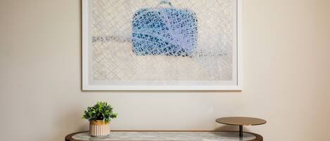 A framed artwork with a geometric pattern, a potted plant, and a round table with a marble top.