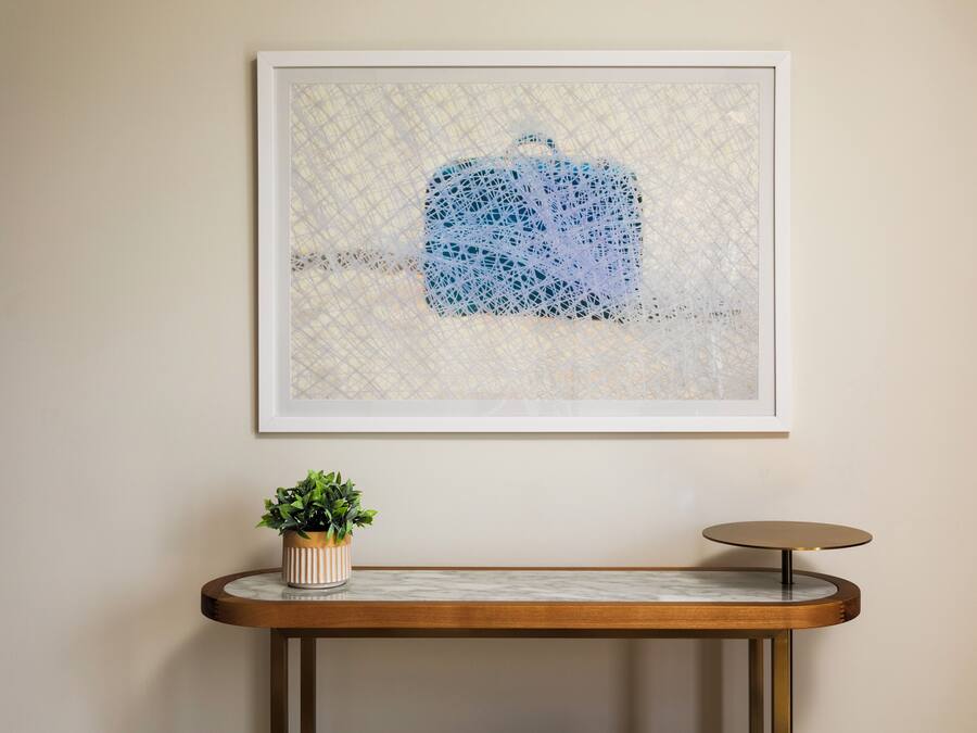 Ein gerahmtes Kunstwerk mit geometrischem Muster, eine Topfpflanze und ein runder Tisch mit Marmorplatte.