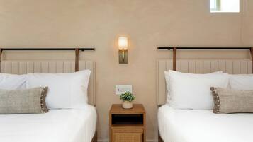 A hotel room with two beds, a nightstand with a lamp, and a small window.