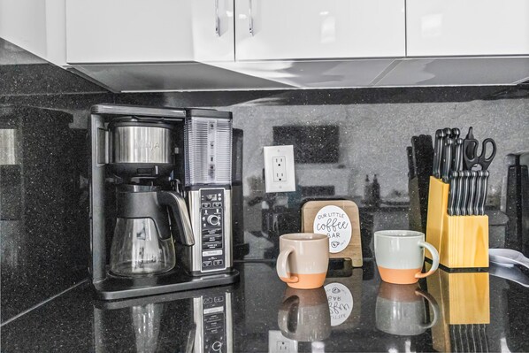 A kitchen with a coffee maker, two mugs, and a knife block on the counter.