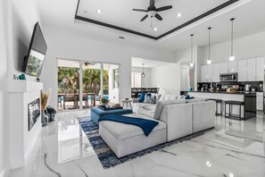 A modern living room with a white sofa, a blue accent piece, and a kitchen area with white cabinets and a microwave.