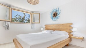 A bedroom with a wooden bed, a large window with curtains, a wall art piece, and a bedside table with a lamp. - Casa Margarita with seaview and pool (Tertenia)