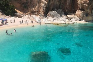 A beach with clear turquoise water, rocky formations, and people swimming and sunbathing.