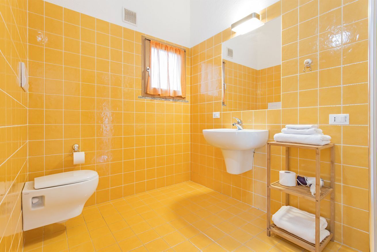 A bathroom with yellow tiles, a toilet, a sink, and a shelf with towels.