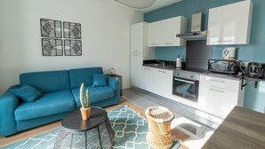 A compact living space with a blue sofa, kitchenette, and a ceiling fan.