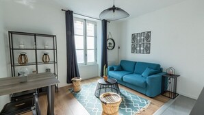 A modern living room with a blue sofa, a dining table with chairs, a coffee table, and a patterned rug.