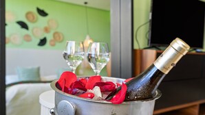 Une bouteille de champagne dans un seau en métal rempli de glace et de pétales de rose, avec deux verres et une bougie en arrière-plan.
