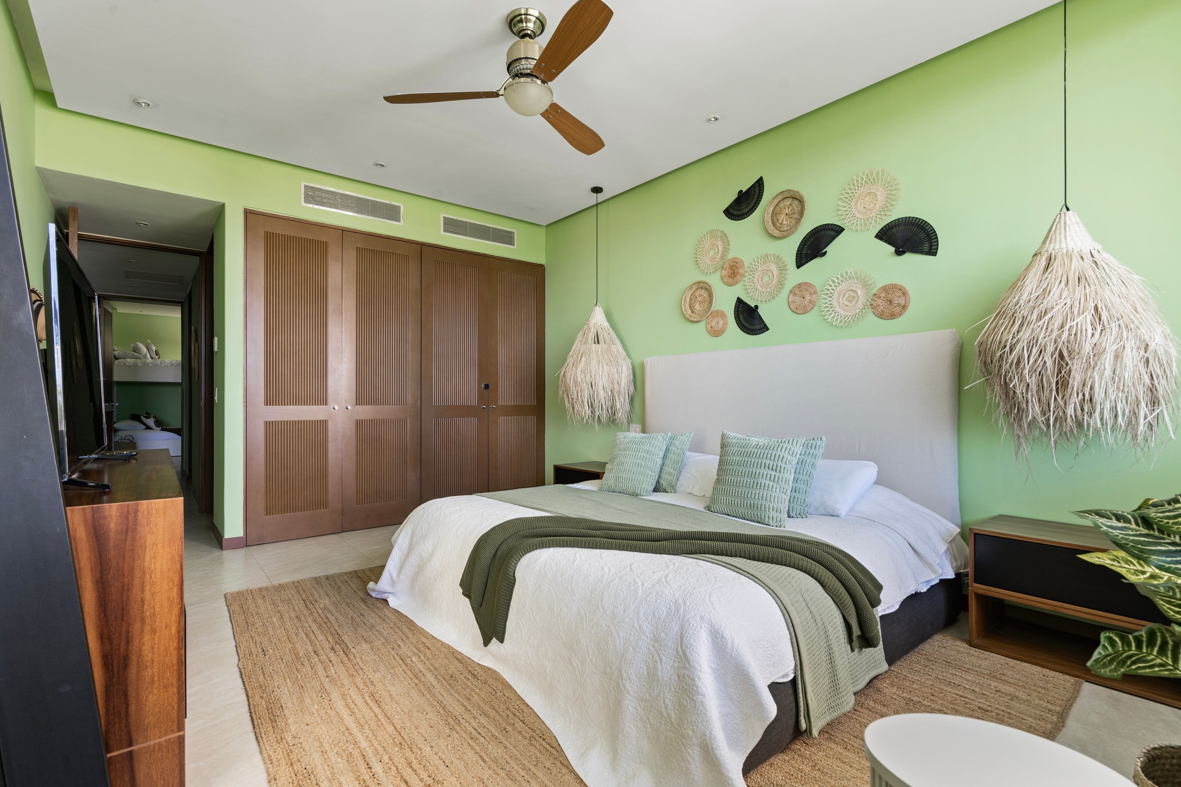 A bedroom with a bed, wooden wardrobe, ceiling fan, wall decor, and a hanging lamp.