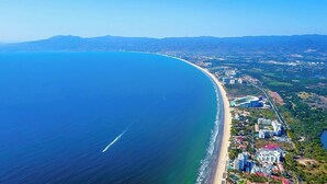 Une vue aérienne d’une zone côtière avec une plage, des bâtiments et des montagnes en arrière-plan.