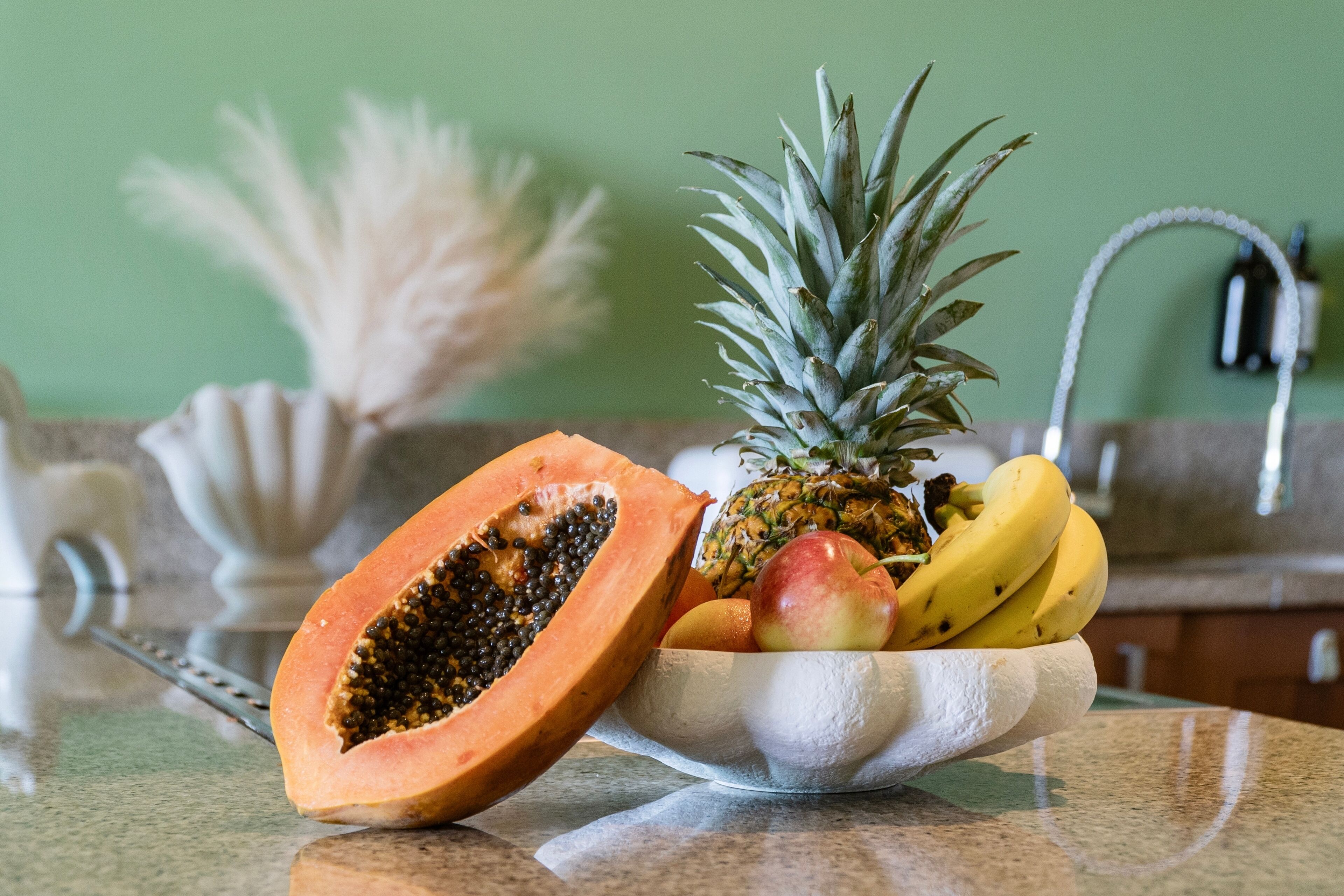 Un bol de fruta sobre una encimera de cocina, con una pared verde al fondo.