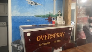 Une pièce ornée d’une fresque représentant un paysage marin, d’un comptoir en bois portant l’inscription « ZONE DE PULVÉRISATION » et d’un mur en briques.