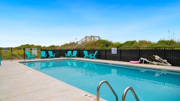 A swimming pool with a black fence, turquoise chairs, and a sign indicating no diving allowed.