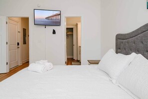 Quarto de hotel com cama, TV fixada na parede e vista para um cais através de uma porta aberta.