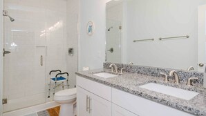 A bathroom with white subway tiles, a glass shower enclosure, a white toilet, and a double sink with a granite countertop.