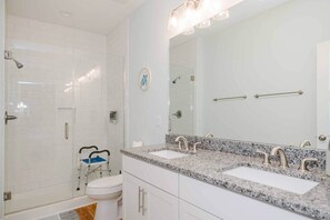 A bathroom with white subway tiles, a glass shower enclosure, a white toilet, and a double sink with a granite countertop.