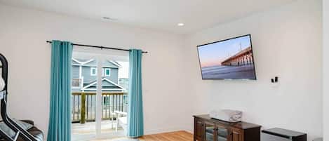 A room with a large sliding glass door leading to a balcony, a flat-screen TV mounted on the wall, a wooden cabinet, and a small refrigerator.