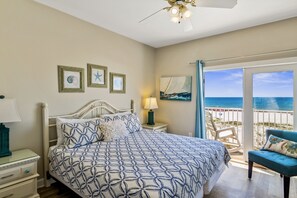 Un dormitorio con cama, mesita de noche, lámpara, silla y vista al océano.
