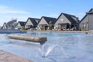 A swimming pool with a stone edge, surrounded by houses with sloped roofs and a clear sky. - Cozy Branson Escape w/ Pool Access, Pvt Hot Tub , & Small-Dog Friendly (Hollister)