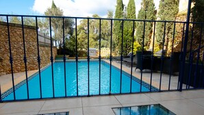 Une piscine rectangulaire avec un mur en pierre d’un côté et une clôture en métal de l’autre.