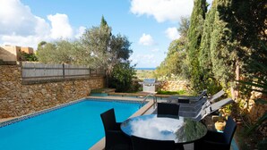 Un espace aménagé au bord de la piscine, avec un mur en pierre, un barbecue et du mobilier d’extérieur.